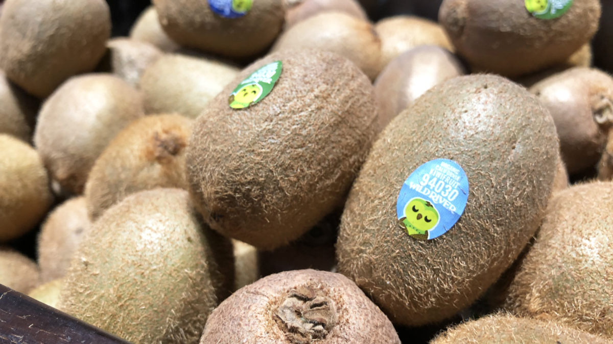 Our Owl Friends and associated kiwi owl logos are trademarks of Wild River Marketing Inc. Designed by Ben Young Landis and Guy Rogers. The photo shows a series of P L U stickers on green kiwifruit stocked at Market 5 One 5 in Sacramento. The stickers read: Organic California Kiwifruit 94030 Wild River, and feature a green kiwi owl.