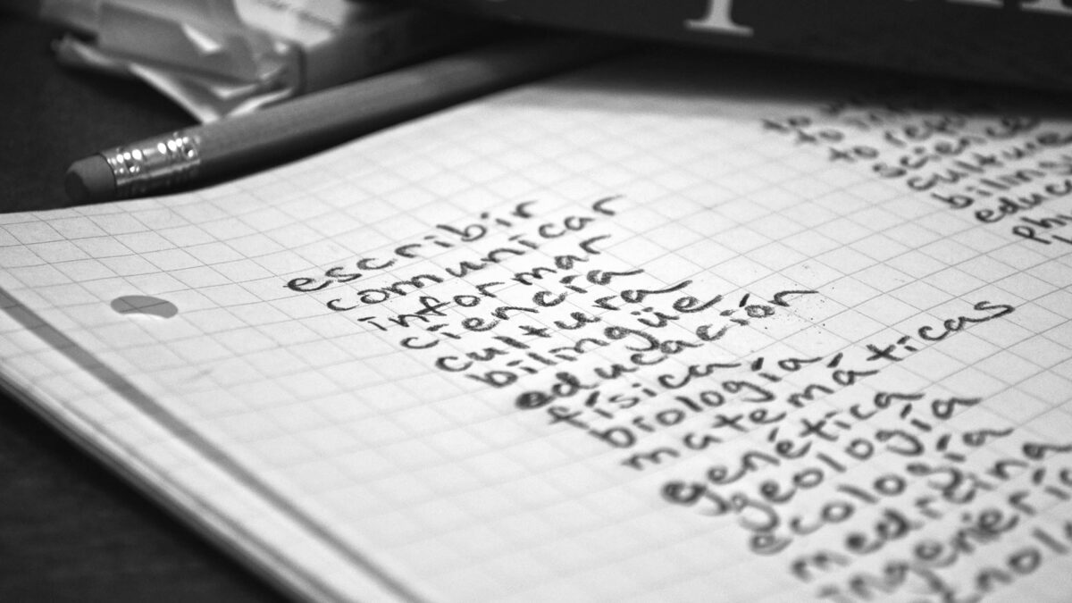 Cover photo for the communicatingciencia.org website. It is a black and white photo of a gridded sheet of paper with a list of penciled words in Spanish, starting with "escribir, comunicar, informar, ciencia, cultura" and so on. A pencil appears in the background. (Graphic by Ben Young Landis)