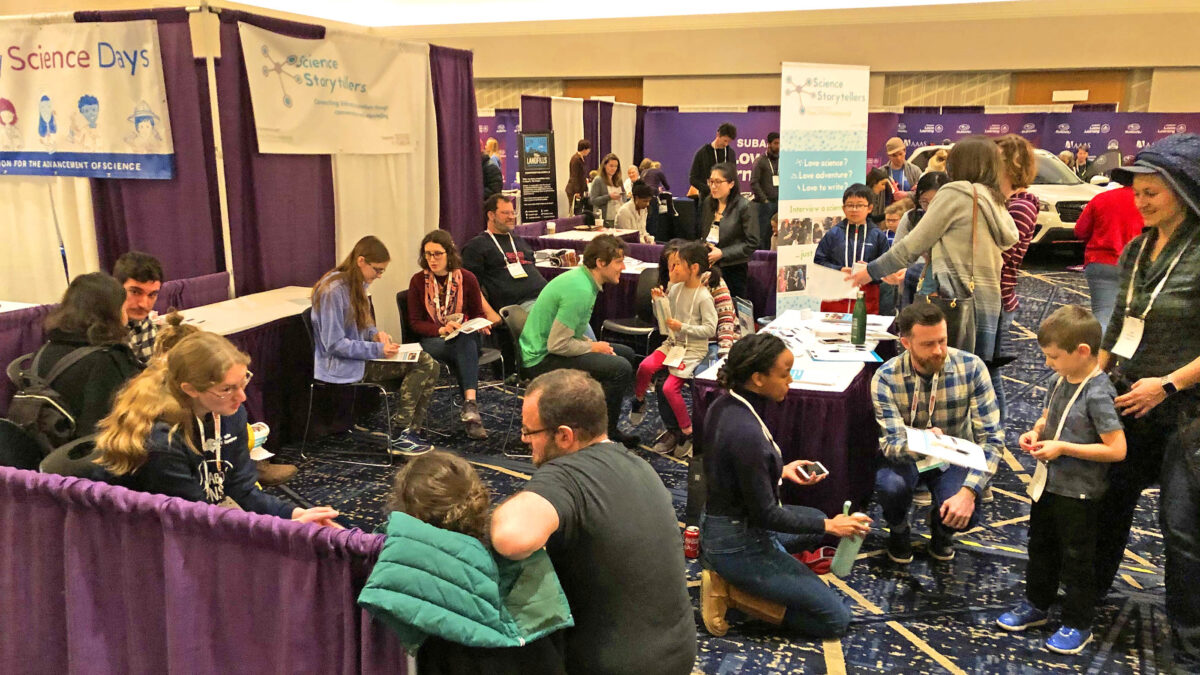 Children and parents gather at the Science Storytellers booth at the Family Science Days public fair hosted in Seattle by the American Association for the Advancement of Science, February 16, 2020. The photo shows scientists of diverse ethnicities and genders seated and being interviewed one-on-one by kids with pen and paper in hand. (Photo by Ben Young Landis for Science Storytellers)