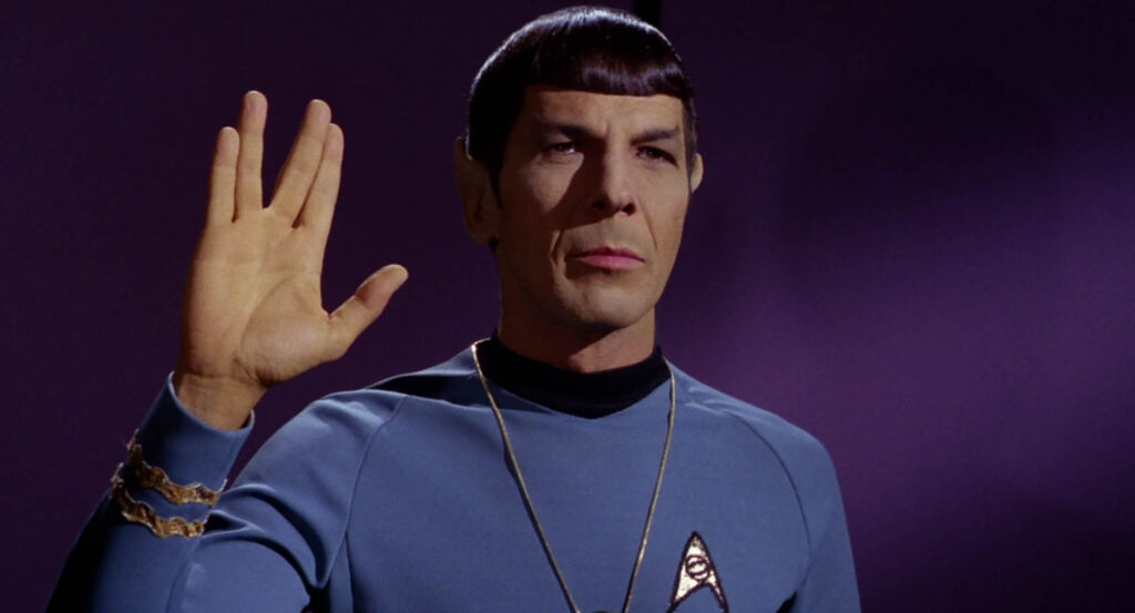 Photo of Mr. Spock from Star Trek, holding his hand up in the Vulcan salute, with a "V" formed by parting his fingers. 