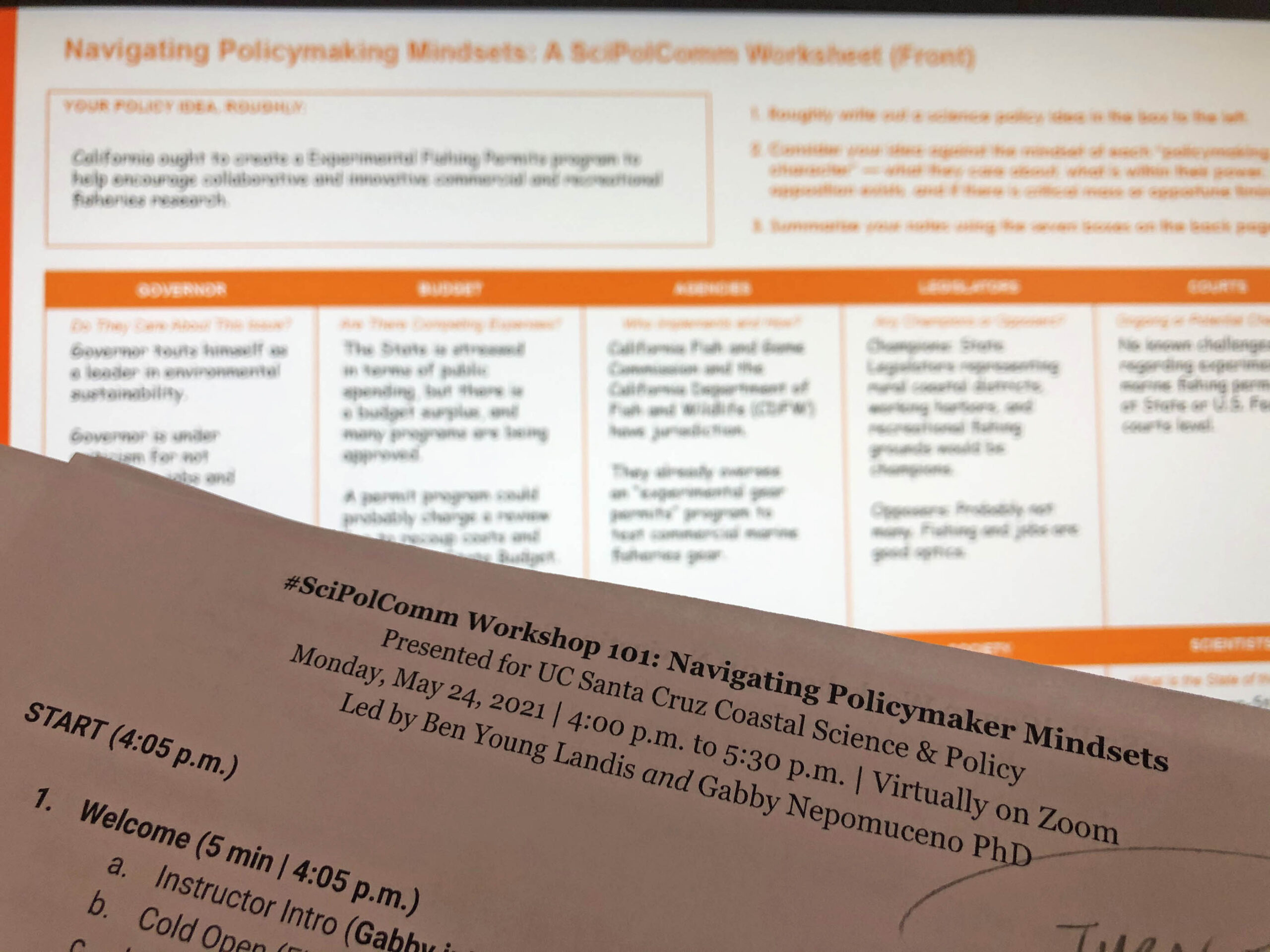 Photo of a course plan on a piece of paper held up to a computer screen, where a gridded worksheet titled Navigating Policymaking Mindsets: A Sci Pol Comm worksheet” can be seen.