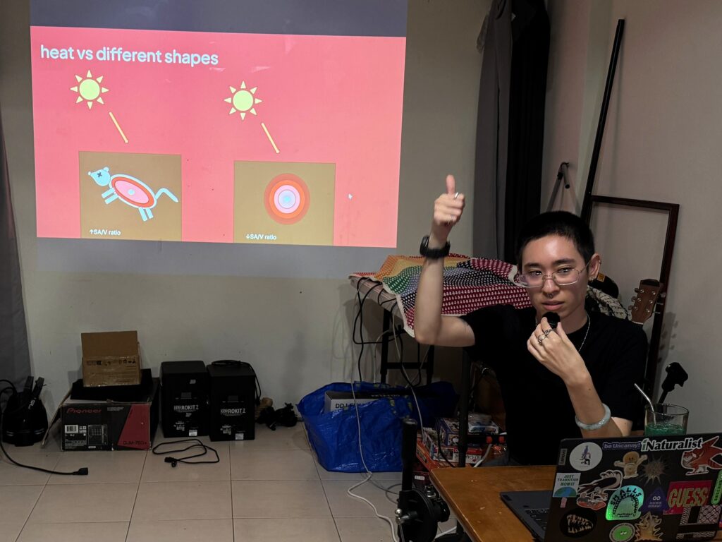 Photo of River Basham giving a thumbs up gesture in front of a slide showing a cartoon dead mouse versus a cartoon ball, both exposed to solar heat
